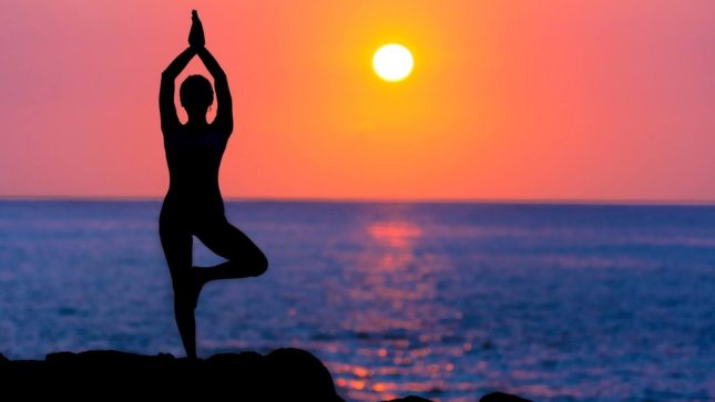 Woman doing yoga at sunset on a beach.