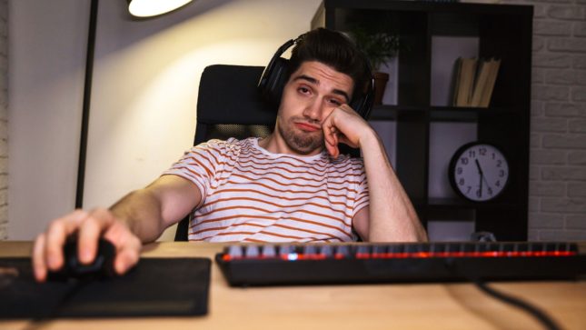 Brown haired, brown eyed man with a headset clicking on a mouse looking apathetic slash bored and is wearing a red and white striped shirt.