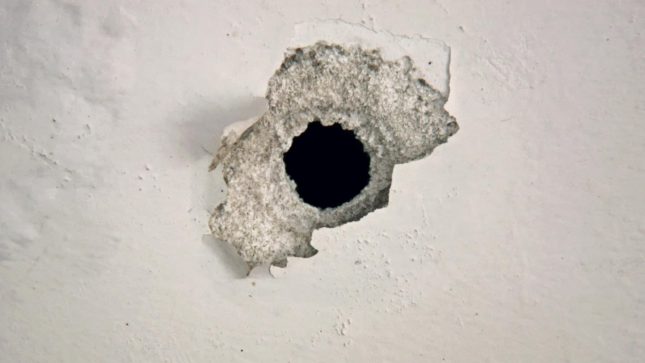 Glory hole in beat up white wall.