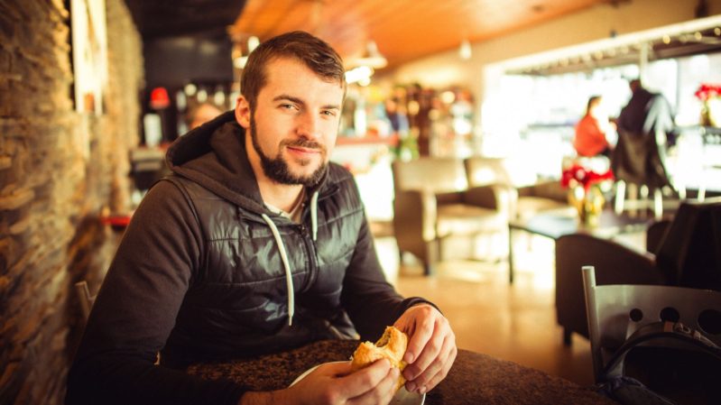 Man in a black sweatshirt and black vest sitting at a bar table looking at the camera.