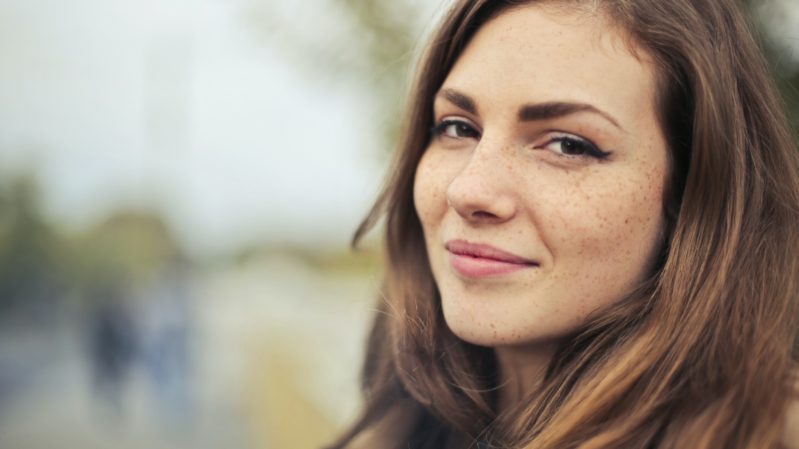 Woman with light brown hair and dark brown eyes grinning with freckles and olive skin tone.