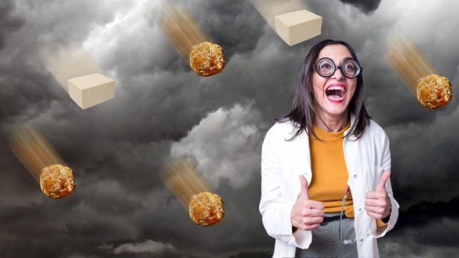 Woman with an excited, open mouth and an orange turtle neck with a white cardigan and circular, hipster glasses, against a cloudy background with vegan meatballs falling from the sky.