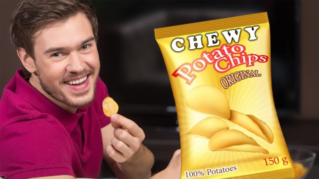 White man with brown hair and blue eyes smiling with a potato chip in his hand. He is in a dark red/maroon collared shirt. Next to him is a big, yellow bag of potato chips that says: "Chewy Potato Chips Original, 100% potatoes, 150 g". The bag has goldish yellow, curved potato chips on it. Both are against a black background.