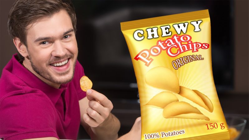 White man with brown hair and blue eyes smiling with a potato chip in his hand. He is in a dark red/maroon collared shirt. Next to him is a big, yellow bag of potato chips that says: "Chewy Potato Chips Original, 100% potatoes, 150 g". The bag has goldish yellow, curved potato chips on it. Both are against a black background.