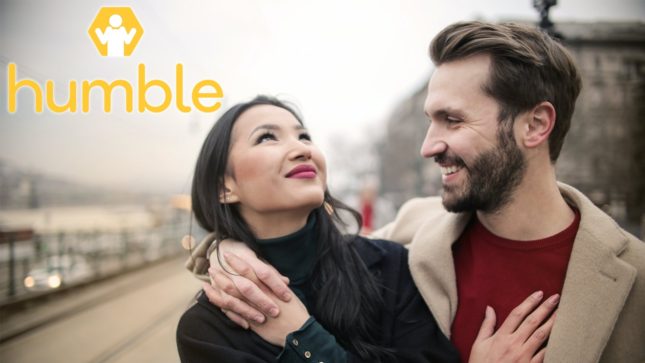 Smiling asian woman with red lips and straight black hair wearing a black turtleneck with her hand on the chest of a smiling ashy white man with brown hair and a brown beard, a red shirt, and a tan jacket, both standing on a gray background road. There's a "Humble" logo with a shrugging yellow and white figure in it.