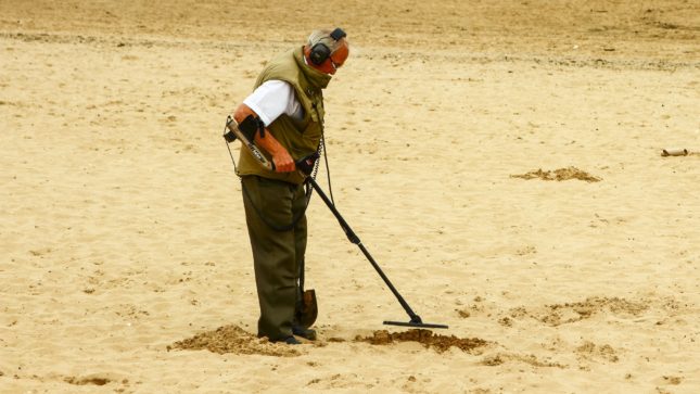 Old, white man at the beach with a metal detector.