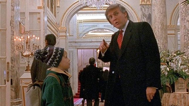 Fat orange man Donald Trump in a black suit and red tie pointing towards the camera. Standing next to him is shorter young boy Kevin McAllister looking up at him in a green jacket and a blue hat that has a pom-pom on top. They are in the St. Regis Hotel which is fancy and white with nice arches.