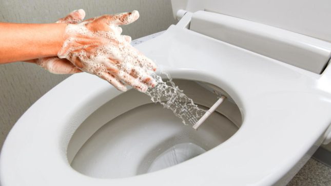 A white person's hands rubbing together over a bidet.