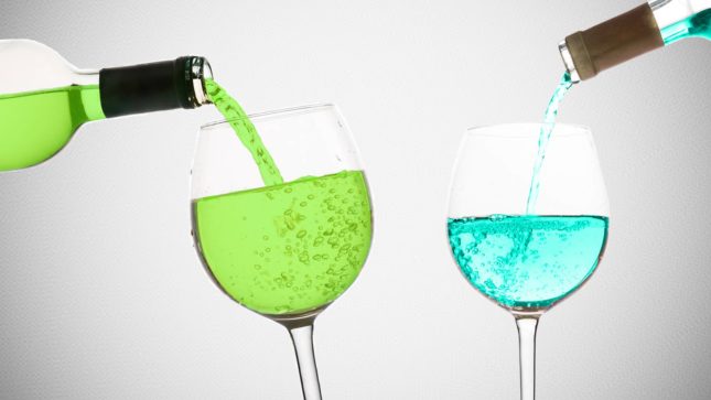 Lime green and turquoise blue wine being poured into clear wine glasses of those two colors against a gray background that becomes darker gray at the corners.
