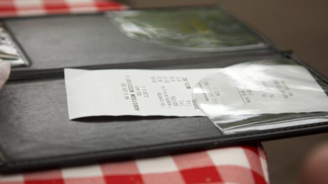 Receipt over a black checkbook on a red and white checkered table cloth. There is a brown hardwood floor behind it.